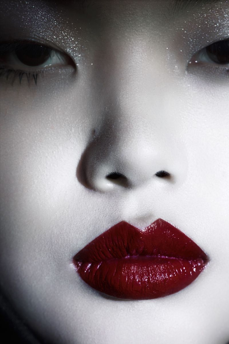 Close-up shot of a person's face with dramatic makeup, focusing on the glossy, deep red lips and glittery eye makeup, high contrast.
