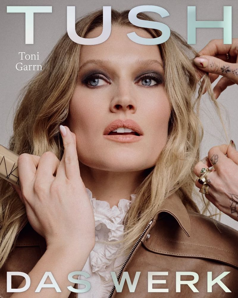 Close-up portrait of blonde model Toni Garrn for TUSH Magazine cover, wearing a brown leather jacket, neutral makeup, and hands near her face.