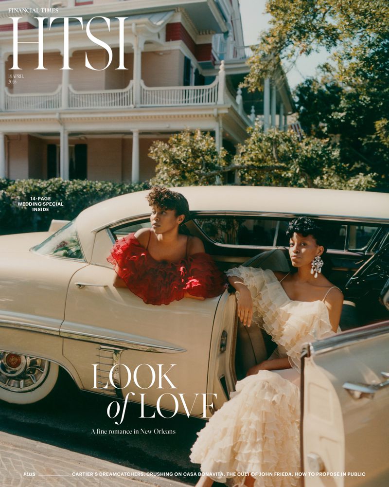 Fashion magazine cover featuring two women in couture gowns inside of a classic car, with a building and foliage visible in the background.