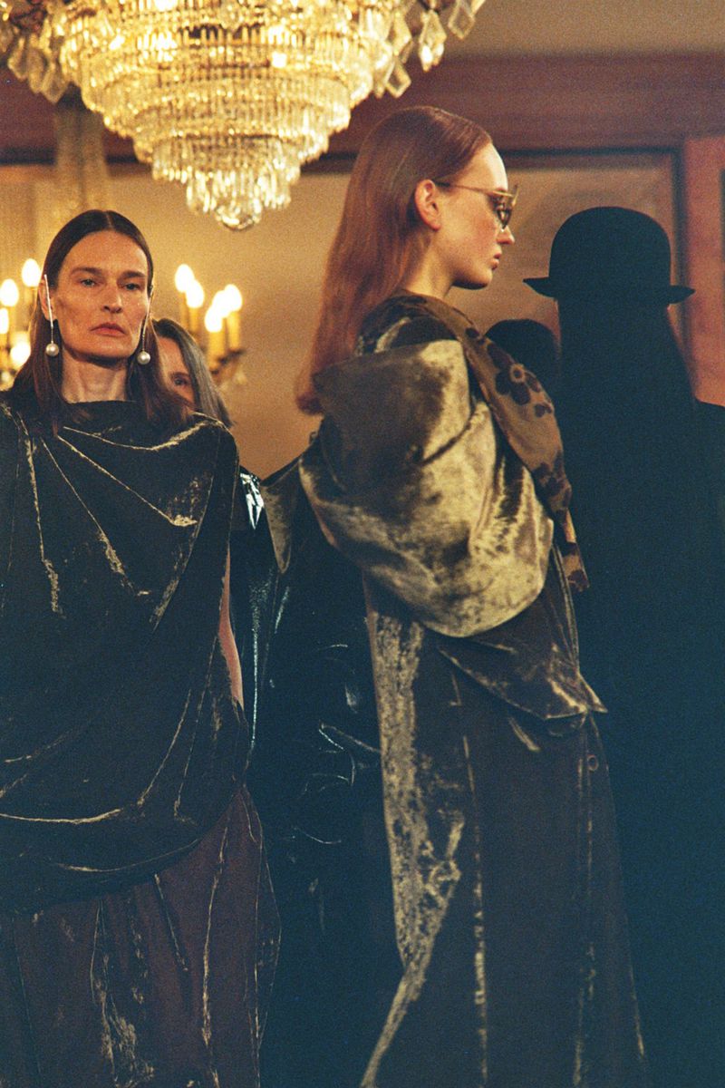 Runway fashion show featuring two women in velvet dresses under chandelier lighting, capturing elegant style and refined atmosphere.
