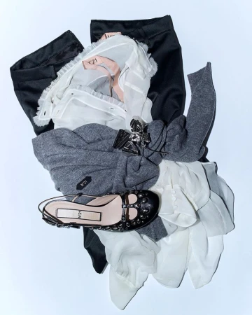 Fashion flat lay featuring a black studded shoe, a grey sweater, a white blouse, and black pants on a white background.
