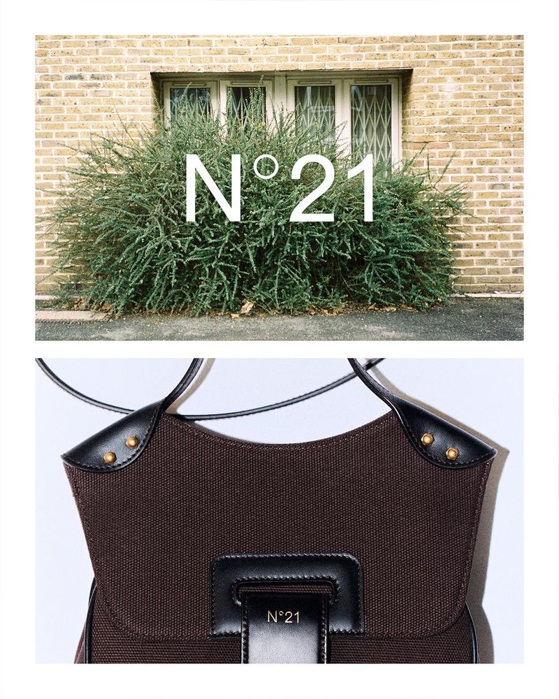 Brown fabric handbag with black leather accents, displayed in front of an exterior brick wall and shrub with 'N°21' text overlay.