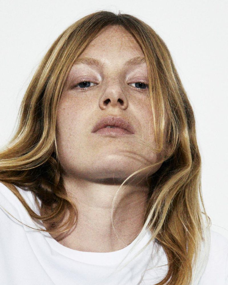 Close-up portrait of a young adult female with freckles and blonde wavy hair, shot in front of a white background in a photo studio.