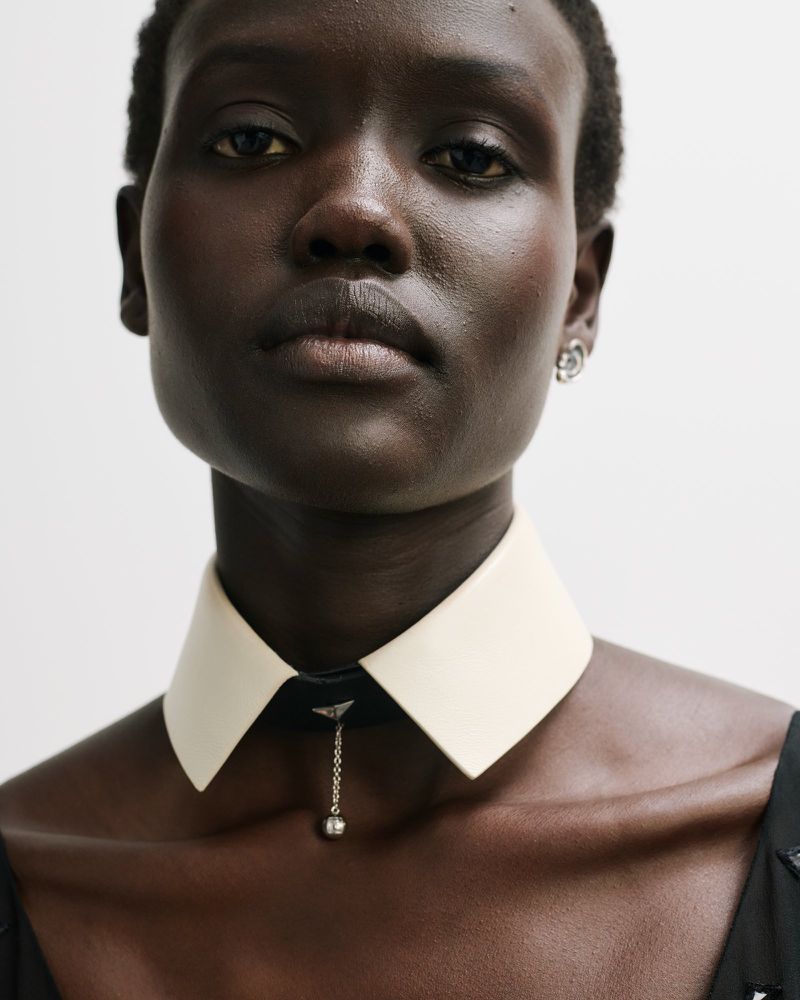 Elegant studio portrait of an African woman with dark skin and a striking white collar necklace against a light background.