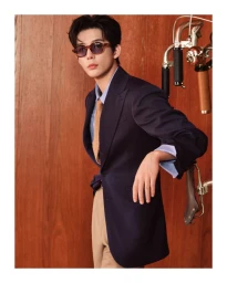 Leo Wu wearing tortoiseshell sunglasses, a navy blazer, and beige trousers against a wood paneled wall for Celine.