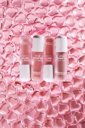 Kylie Cosmetics lip gloss products sit among many pink, translucent heart-shaped objects on a pink background in a studio shot.