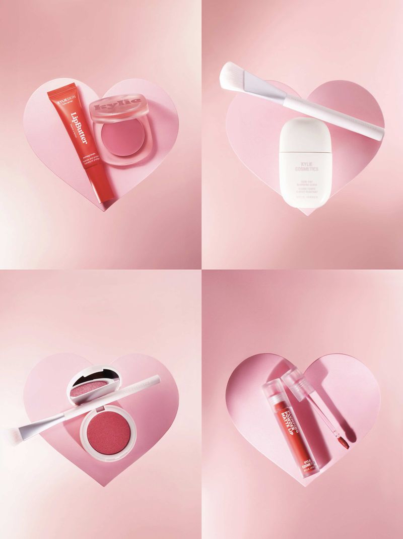 Cosmetic product still life: lipstick, blush, and applicator brush arranged in a pink background with heart-shaped cutouts.
