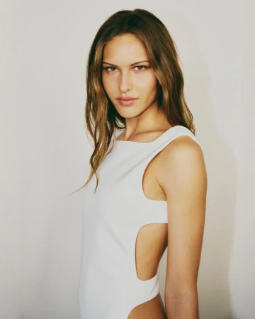 Model wearing a white sleeveless cut-out dress posing against a plain backdrop backstage at Courrèges.