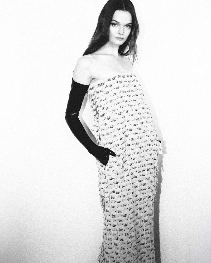 A fashion portrait of a young woman wearing a patterned dress and long gloves against a white background in a studio setting.