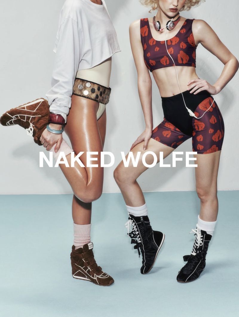 Two women posing in 80s-inspired athleisure wear, featuring crop tops, shorts, leggings, and high-top sneakers, with a pale blue background.