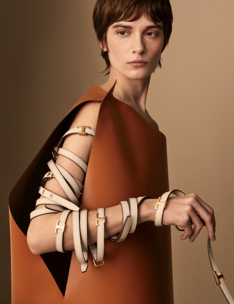 Fashion shot of a woman wearing a brown garment and multiple cream-colored bracelets with gold hardware in a studio setting.