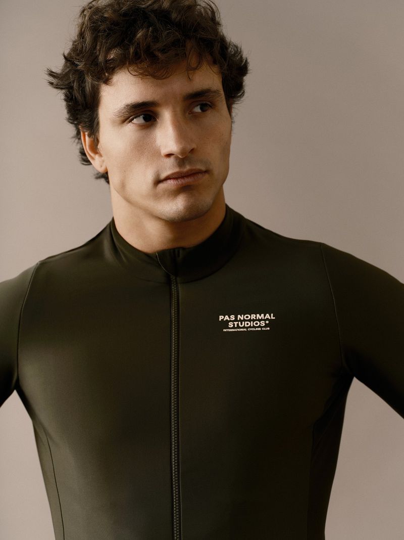 Portrait of a man in a form-fitting, long-sleeve, olive-green athletic top with a front zipper, showcasing athletic fashion.