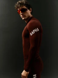 Sergio Modrego wearing a burgundy Rapha long-sleeve cycling skinsuit and shield sunglasses against a dark background.