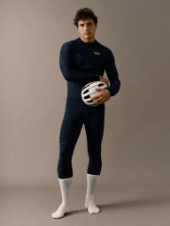 Model Sergio Modrego standing in a dark navy long-sleeve cycling kit holding a white helmet against a neutral backdrop.