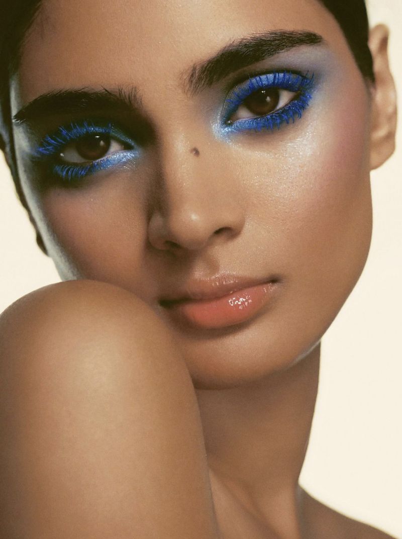 Close-up studio shot of a woman with blue eyeshadow and glossy lips, showcasing makeup artistry and beauty trends.