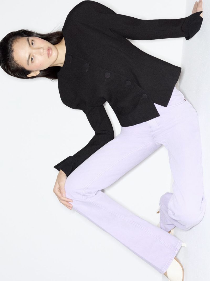 Fashion shot of an adult woman posing in a black jacket and light purple jeans against a white backdrop, showcasing modern style and design.