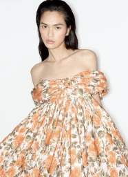 Model Qun Ye wearing an off-the-shoulder orange floral print dress against a plain white studio backdrop.