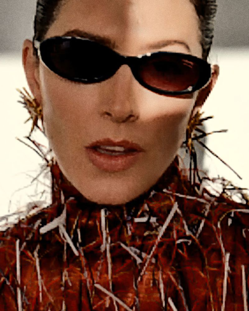 Close-up portrait of Barbara Lennie wearing black oval sunglasses, spiky statement earrings, and a textured high-neck garment.