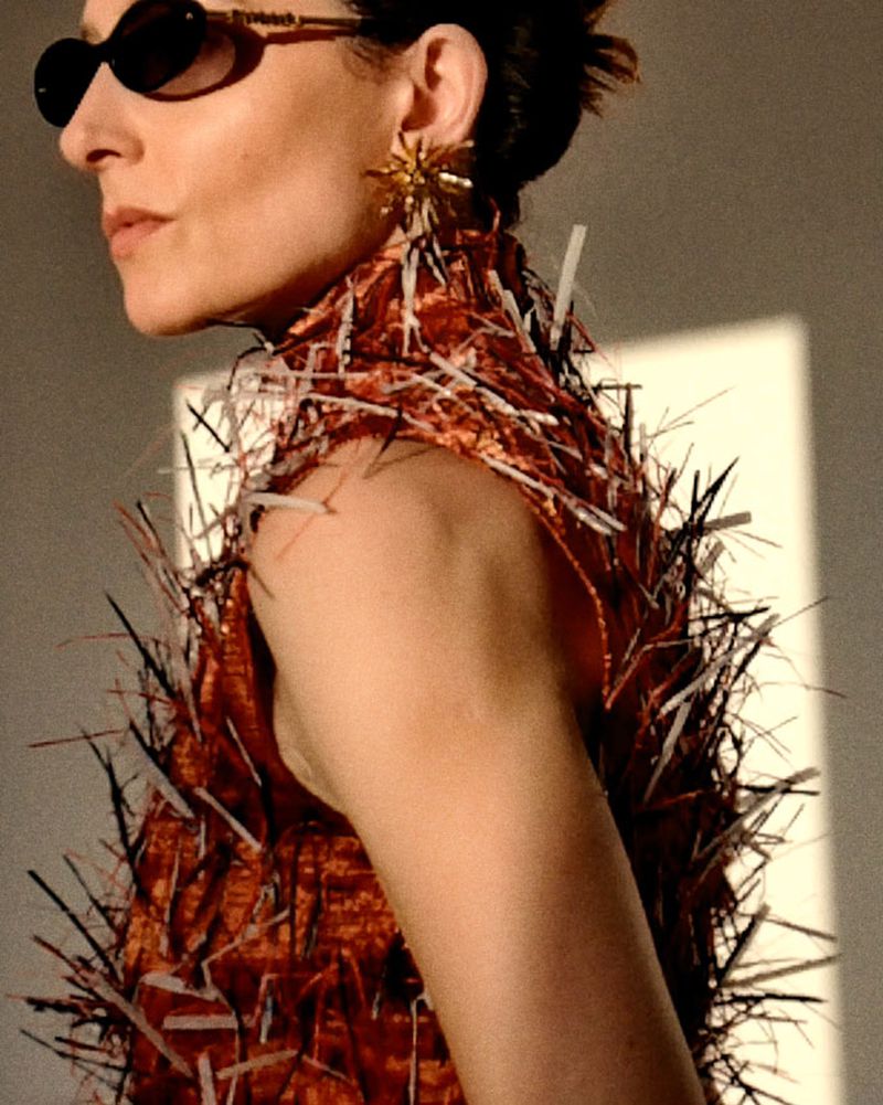 Woman in avant-garde fashion with spiky dress and statement earrings in a high-fashion editorial style, neutral backdrop with soft light.