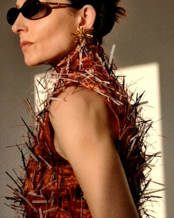 Woman in avant-garde fashion with spiky dress and statement earrings in a high-fashion editorial style, neutral backdrop with soft light.