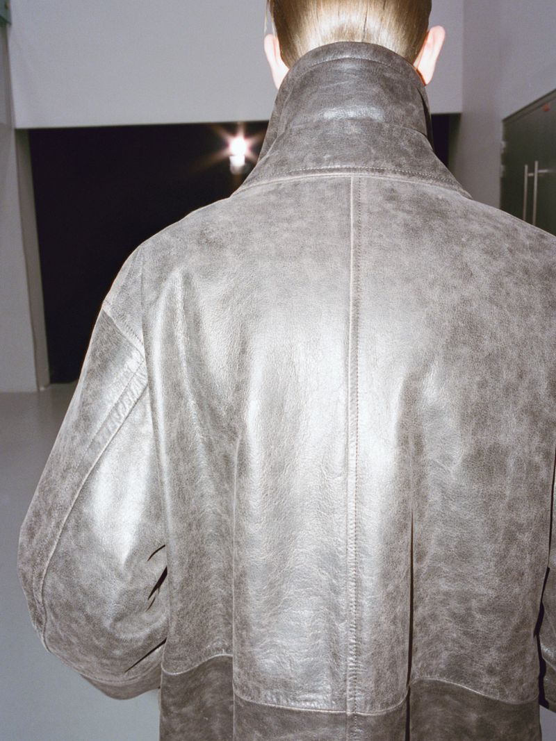 Back view of a person in a gray overcoat against a modern interior with cool lighting and neutral colors. Fashion editorial.