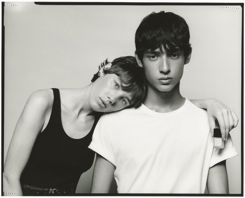 Monochrome portrait of two models in a studio setting, one in a black tank top, the other in a white t-shirt, posing closely together.