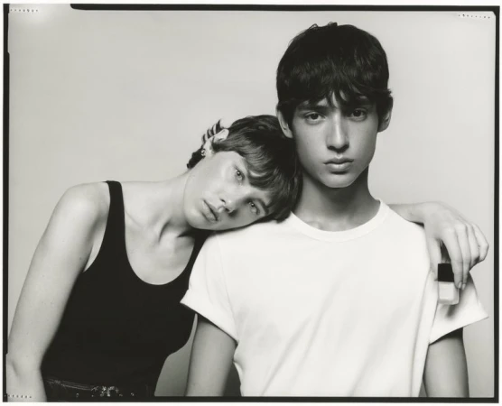 Monochrome portrait of two models in a studio setting, one in a black tank top, the other in a white t-shirt, posing closely together.