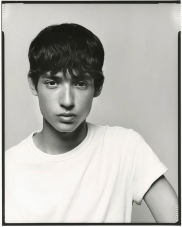 Portrait of a young adult with dark hair and light skin in a white t-shirt against a neutral background in a black and white photograph.