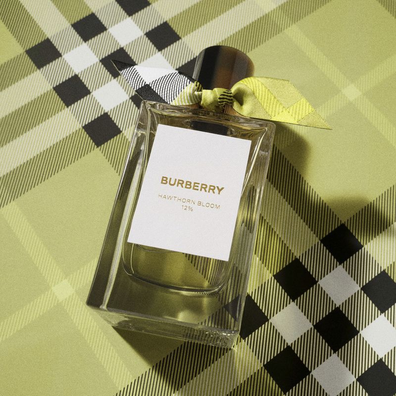 Burberry Hawthorn Bloom perfume bottle sits diagonally on a lime green, white, and black plaid surface with a ribbon detail.