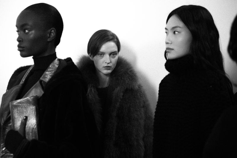Monochrome shot of three fashion models posing in dark clothing against a white backdrop, emphasizing textures and minimalist aesthetic.