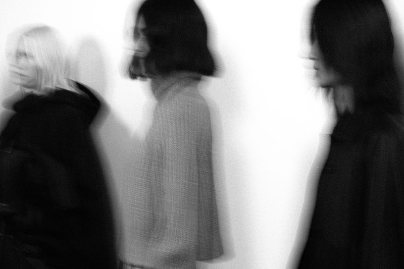Three blurred women stand close together, conveying a sense of motion and artistic expression in a black and white medium shot.