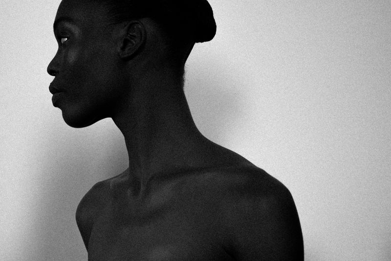 Monochromatic close-up portrait of an androgynous Black person in profile against a plain gray background with soft, diffused lighting.