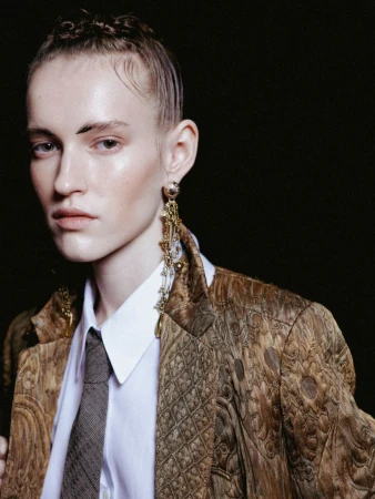 Portrait of adult female with patterned blazer, collared shirt, and tie against a dark background in a fashion editorial style.