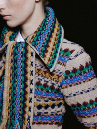Close-up shot of a fair-skinned person with a patterned tan cardigan with blue, yellow, and green on a dark background.