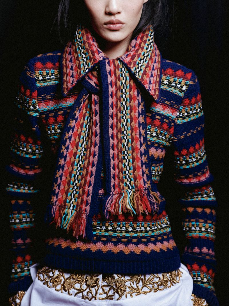 Close-up studio shot of a stylish Asian woman wearing a colorful patterned sweater and scarf with a decorative white skirt.