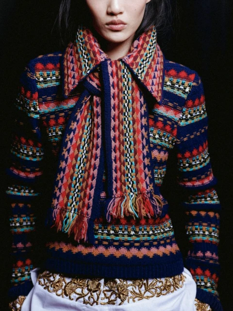 Close-up studio shot of a stylish Asian woman wearing a colorful patterned sweater and scarf with a decorative white skirt.