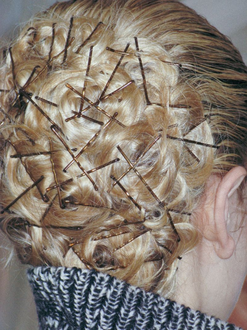 Close-up on a person with blonde hair styled with multiple brown bobby pins scattered throughout the curls, adding texture and hold.