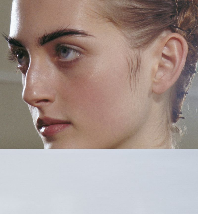 Close-up portrait of a young adult woman with fair skin, light eyes, and light brown hair styled up, set against a neutral backdrop.