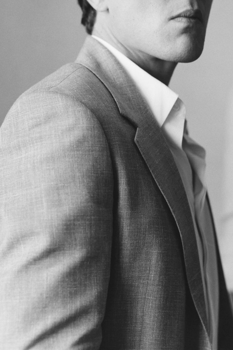Close-up shot of an adult male's torso in a light gray suit and white dress shirt against a gray background, showcasing fashion and tailoring.