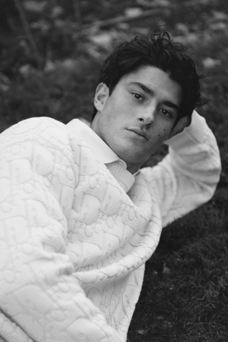 Black and white portrait of a handsome young man lying on the grass, wearing a patterned sweater, looking thoughtfully at the camera.