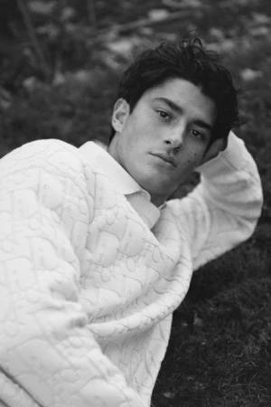 Black and white portrait of a handsome young man lying on the grass, wearing a patterned sweater, looking thoughtfully at the camera.