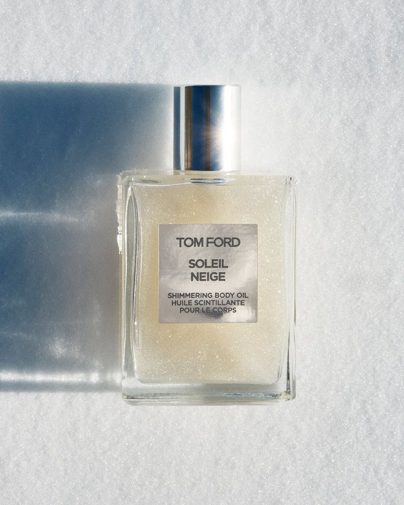 Tom Ford Soleil Neige shimmering body oil in a square glass bottle against a bright, textured white background, with a shadow.