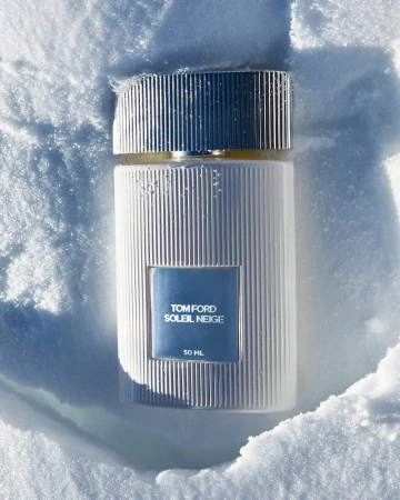 Tom Ford Soleil Neige fragrance bottle, showcasing ribbed design and blue label, nestled in fluffy snow. Beauty and luxury perfume product.
