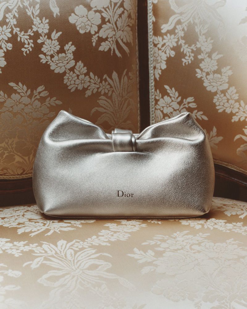 Silver Dior clutch with a bow-like top sits on a patterned surface, creating an elegant and fashionable composition.