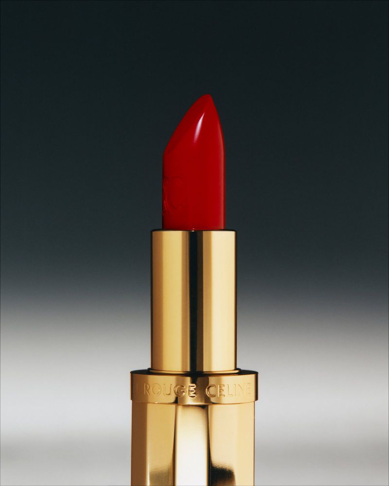 Close-up studio shot of a red lipstick with a gold tube on a gray background, highlighting its color and elegant design.