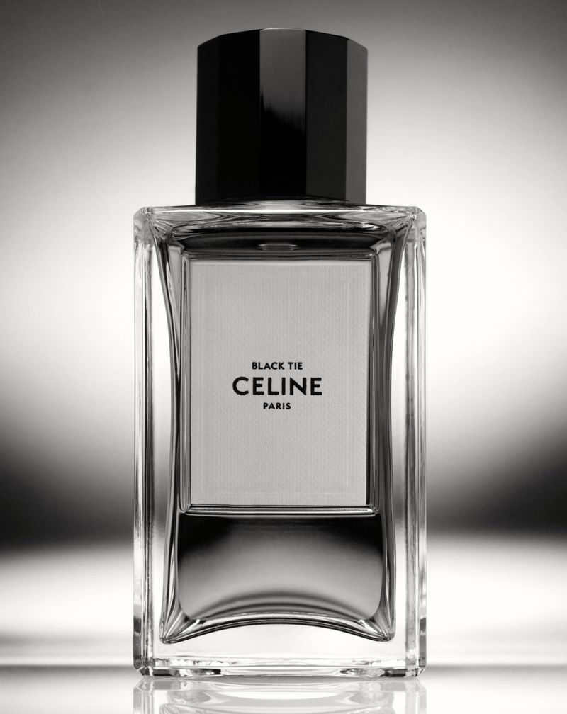 Celine Black Tie fragrance in a clear glass bottle with a black cap on a reflective gray surface in a studio setting.
