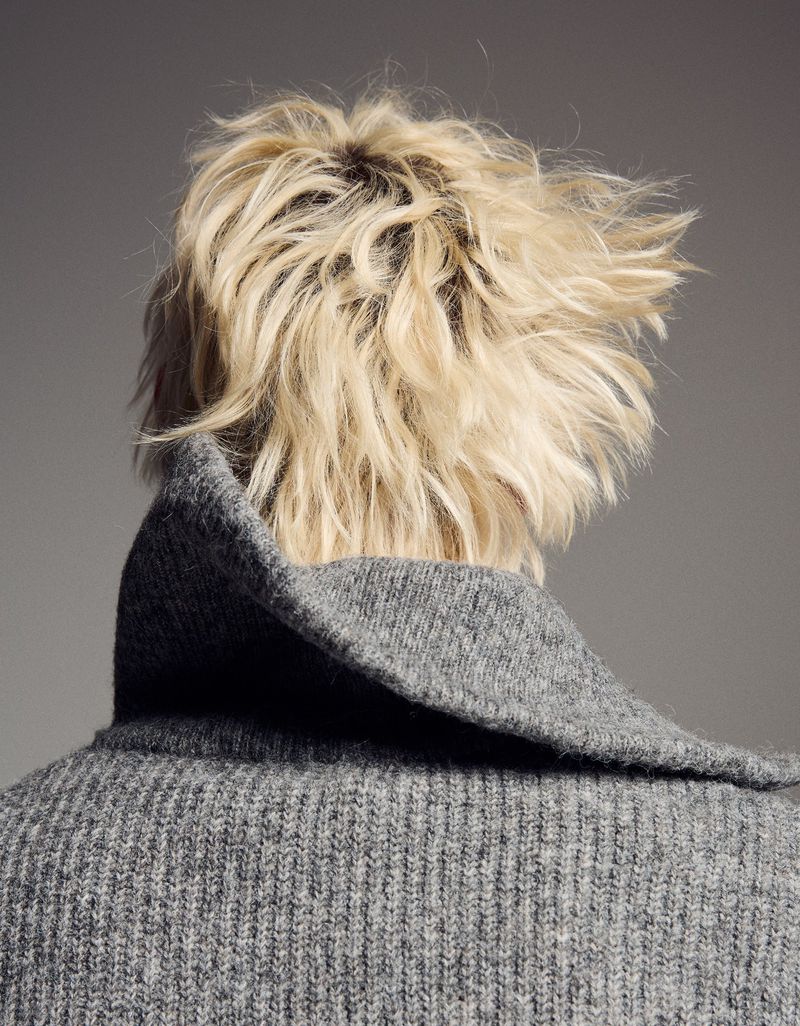 Close-up back shot of a person with blonde hair wearing a gray knit sweater. The focus is on the texture of the knit and the hairstyle.