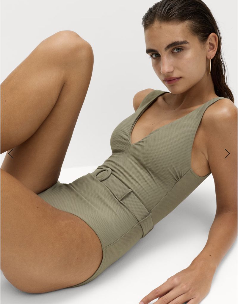 A young woman in a green, one-piece swimsuit poses against a white background, showcasing swimwear fashion and beauty.