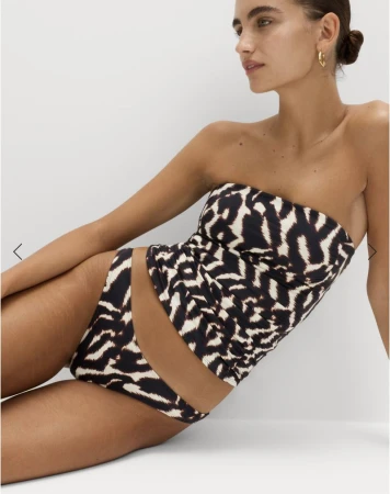 Adult woman poses in a black-and-white patterned bikini. She wears gold hoop earrings with a white background.