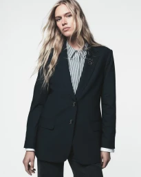 Model Nikki McGuire wearing a black tailored blazer and striped collared shirt against a white seamless backdrop for DKNY SP26.